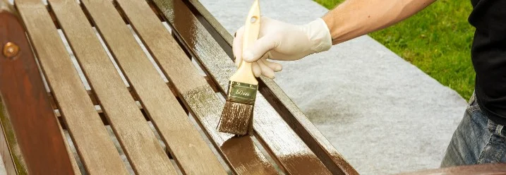 Person lasiert Holzbank mit Pinsel.